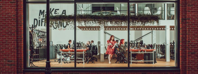 Panoramic shot of the IE studio, taken through the windows. Members of the team are seen working at their desks. 