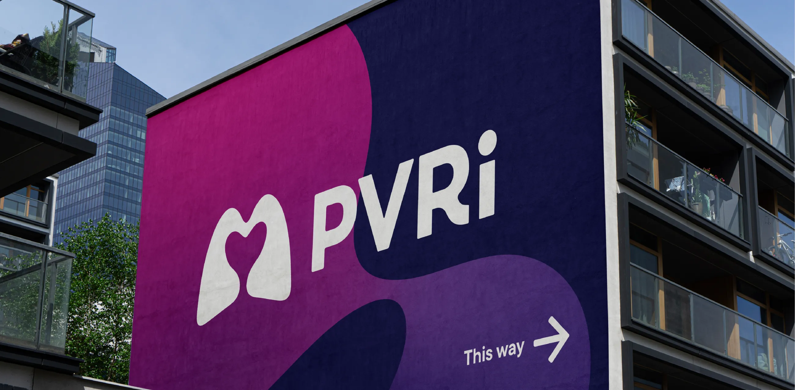 Huge PVRI signage on the side of a building. PVRI logo in white on a background of a signature fluid shape in shades of pink, plum, purple and indigo. With an arrow showing people the event is 'This way'